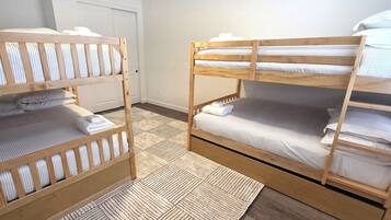Een kamer met twee stapelbedden, een houten vloer en een witte deur op de achtergrond.