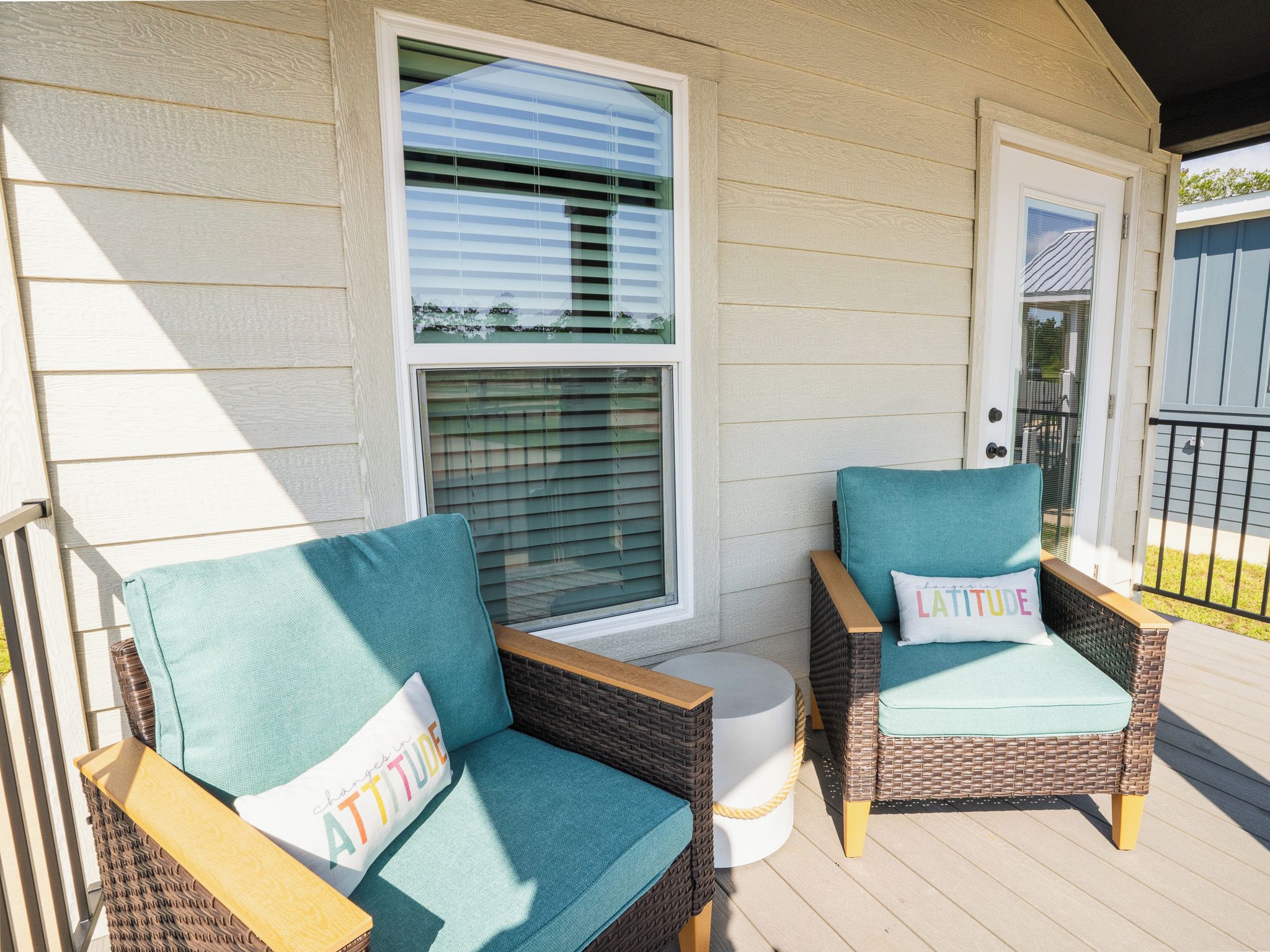 A porch with two wicker chairs, a white door, and a window with blinds.
