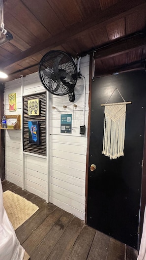 A room with a wooden ceiling, a black door with a macrame decoration, a wall-mounted fan, and a QR code sign. - Eco Hostal Paraiso (Santa Marta)