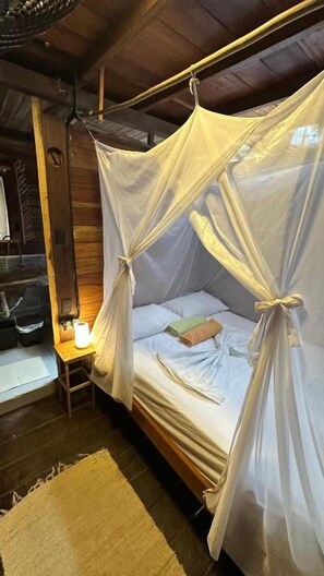 A bed with a canopy, a bedside table with a lamp, and a wooden floor. - Eco Hostal Paraiso (Santa Marta)