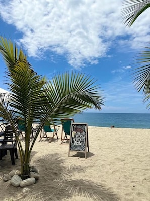 Una playa con palmeras, un letrero y sillas de playa.