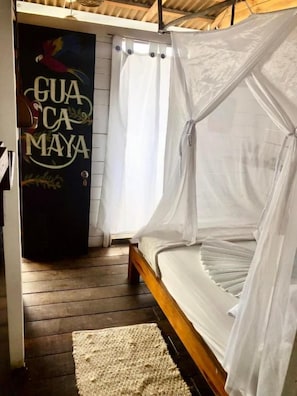 Una habitación con una cama cubierta por una mosquitera, suelo de madera y una pared con un mural.