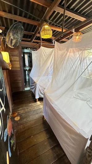 Un pasillo estrecho con una cama cubierta con sábanas blancas, un ventilador y una lámpara colgante.