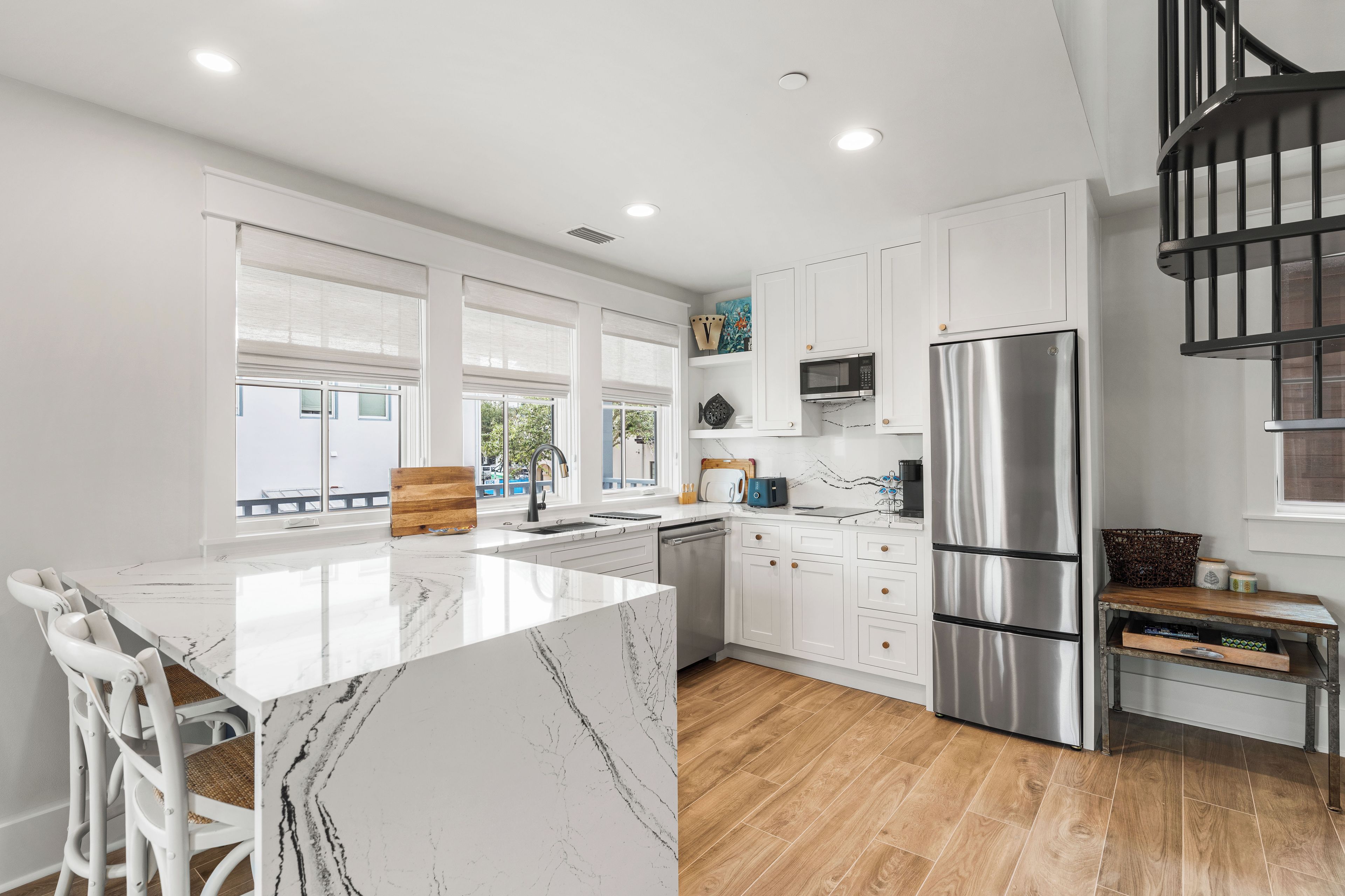 A modern kitchen with white cabinetry, a marble island, and a stainless steel refrigerator.