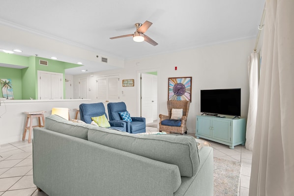 A living room with a sofa, two armchairs, a television, and a ceiling fan. - Beachfront 2BR @ Palm Beach Resort • Sleeps 7 • Stunning Views (Orange Beach)