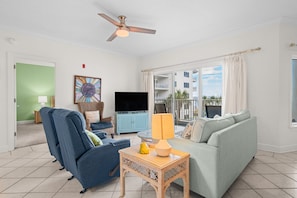 A living room with a sofa, a blue armchair, a television, and a ceiling fan. - Beachfront 2BR @ Palm Beach Resort • Sleeps 7 • Stunning Views (Orange Beach)