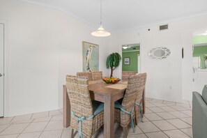 Un coin repas avec une table en bois, des chaises en osier, un panier de fruits et un luminaire suspendu.