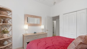 Ein Schlafzimmer mit Bett, Kommode, Spiegel und Tür.