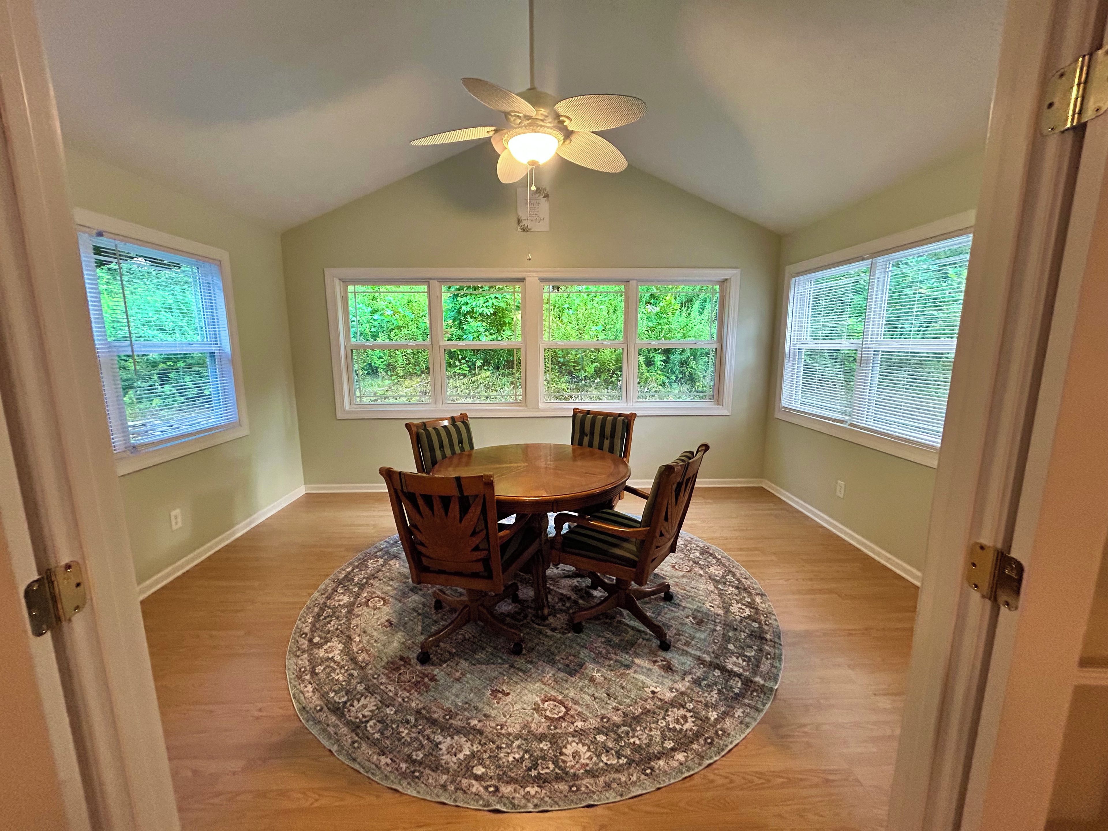 A dining room with a round table, chairs, a patterned rug, and a ceiling fan.