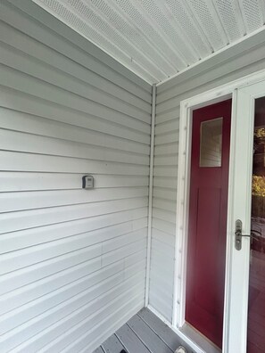 A corner of a building with white siding and a red door.