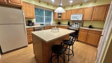 A kitchen with wooden cabinets, a central island with bar stools, a refrigerator, a stove, and a window with blinds.