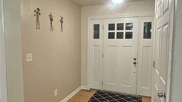 A hallway with a wooden floor, a white door with glass panels, and a black and white rug.