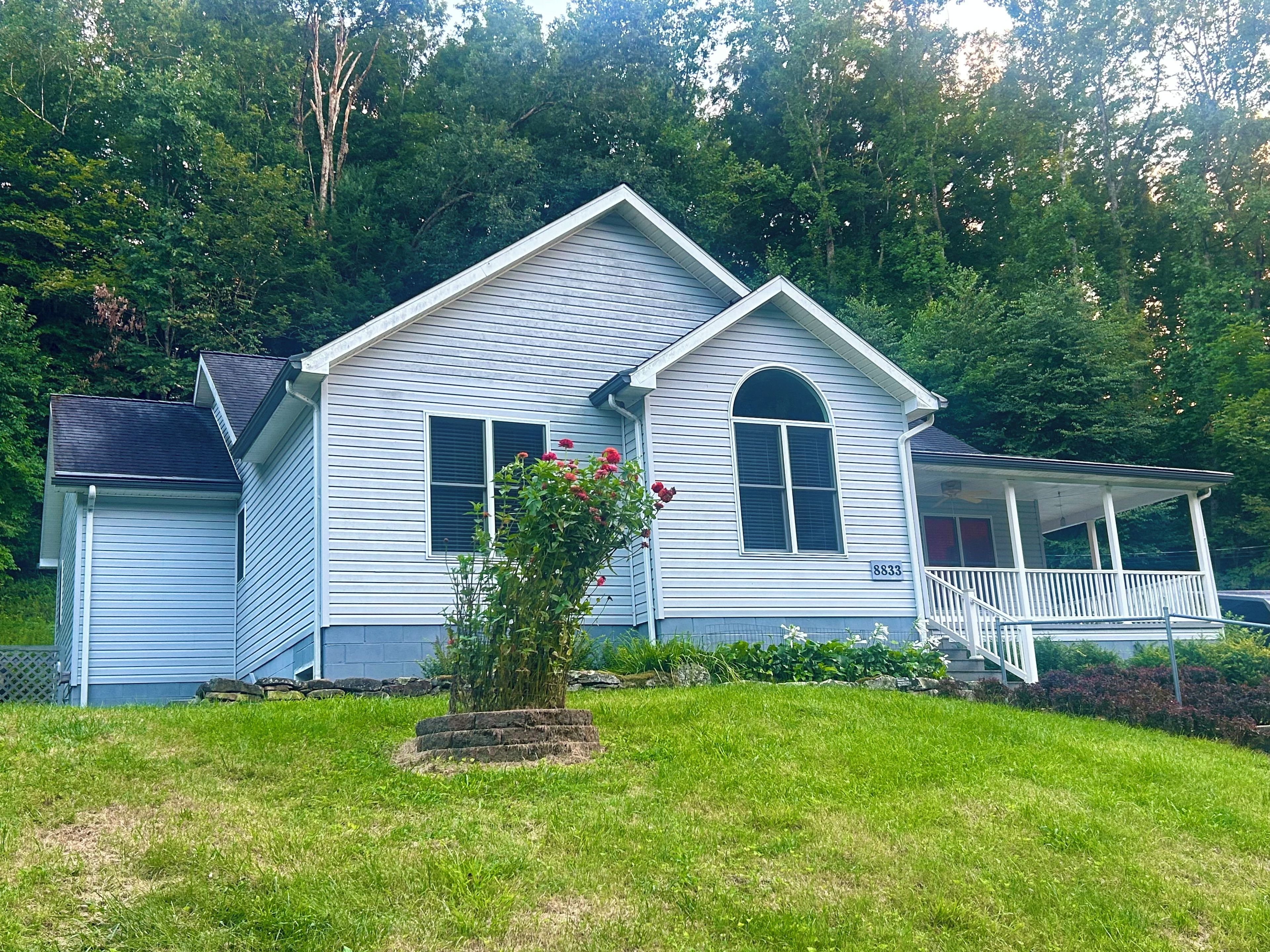A two-story house with a porch, a small garden with a flower bush, and a mailbox.