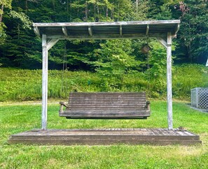 Una panchina di legno sotto una pergola in metallo in una zona erbosa, con alberi sullo sfondo.