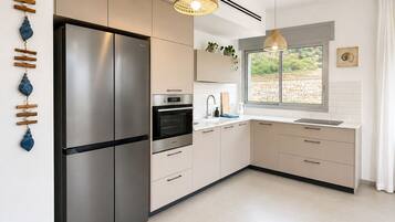 Una cocina moderna con un refrigerador de acero inoxidable, horno y microondas integrado. Hay dos lámparas colgantes, una ventana con vistas y un lavabo con encimera.