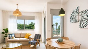 Un soggiorno moderno con divano, poltrona, tavolino rotondo, tavolo da pranzo con sedie e lampadari a sospensione.