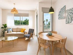 Una sala de estar moderna con sofá, sillón, mesa redonda de centro, mesa de comedor con sillas e iluminación colgante.