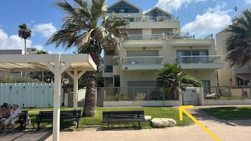 Un immeuble résidentiel à plusieurs étages, doté de balcons, d’un espace de repos couvert et d’un chemin piétonnier dallé.
