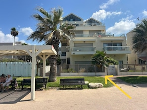 Un edificio residencial de varios pisos con balcones, una zona de estar cubierta y un sendero pavimentado.