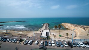 Un parcheggio sulla costa con auto, un molo e una spiaggia con una frangiflutti rocciosa.