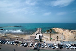 Un aparcamiento costero con coches, un muelle y una playa con rompeolas rocosas.