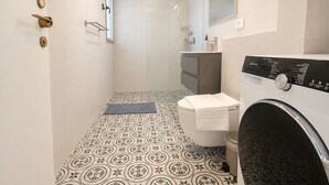 Un bagno moderno con pavimento decorato, un water, una lavatrice e una doccia.