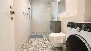 Une salle de bain moderne avec un carrelage décoratif, des toilettes, un lave-linge et une douche.