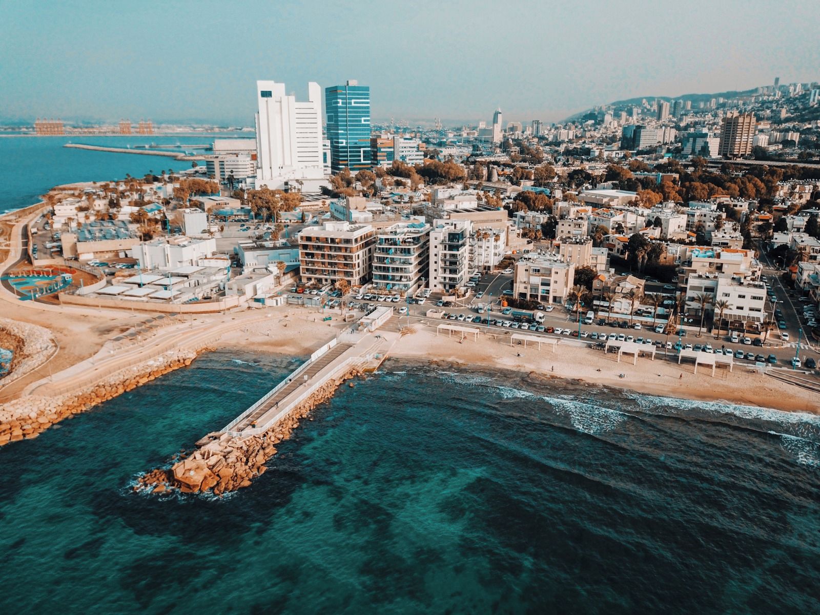 Vue aérienne d’une ville côtière caractérisée par une urbanisation dense, une promenade en bord de mer très fréquentée et une digue rocheuse.