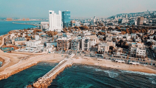 Una vista aerea di una città costiera con un intenso sviluppo urbano, un'elegante passeggiata sul lungomare e un molo frangiato da rocce.