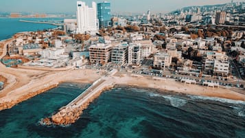 Vue aérienne d’une ville côtière caractérisée par une urbanisation dense, une promenade en bord de mer très fréquentée et une digue rocheuse.