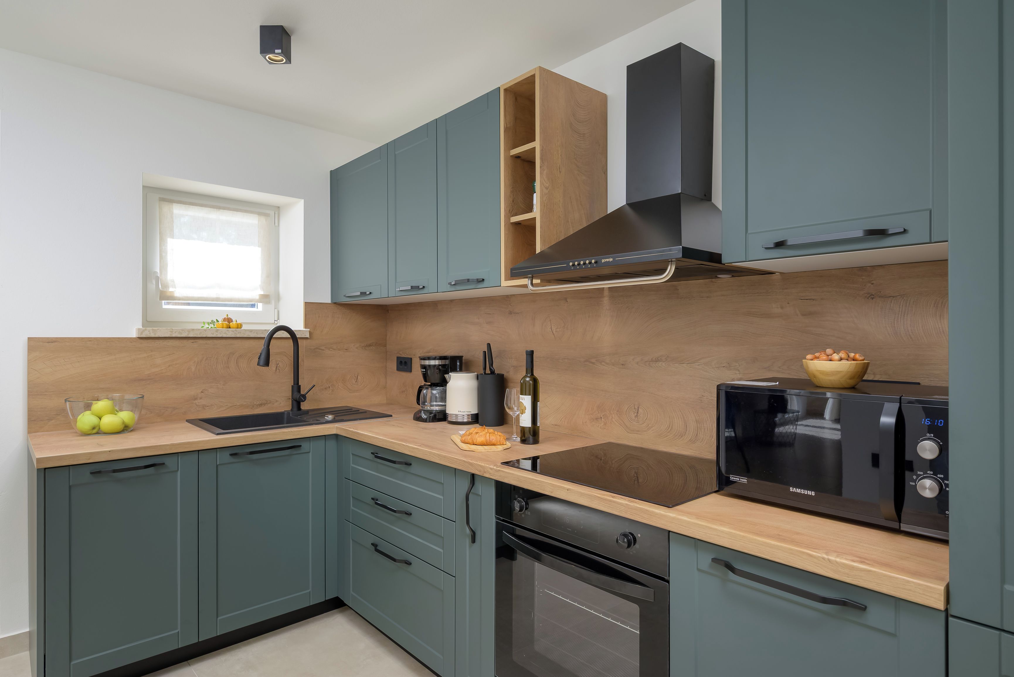A modern kitchen with teal cabinets, a black stove, and a built-in oven.