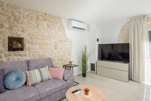 A living room with a stone wall, a grey sofa, a television, and a small table with a remote control. - Villa Merklin (Istria - Debeljuhi) (Debeljuhi)