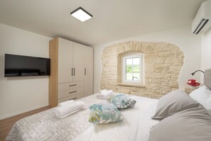 A bedroom with a stone wall, a bed with pillows, a TV, and a window. - Villa Merklin (Istria - Debeljuhi) (Debeljuhi)