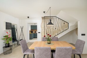 A modern dining area with a wooden table, grey upholstered chairs, a black pendant light, and a staircase with a geometric wall design. - Villa Merklin (Istria - Debeljuhi) (Debeljuhi)