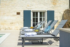 A row of sun loungers with towels and a fruit bowl, set against a stone wall with a door in the background. - Villa Merklin (Istria - Debeljuhi) (Debeljuhi)