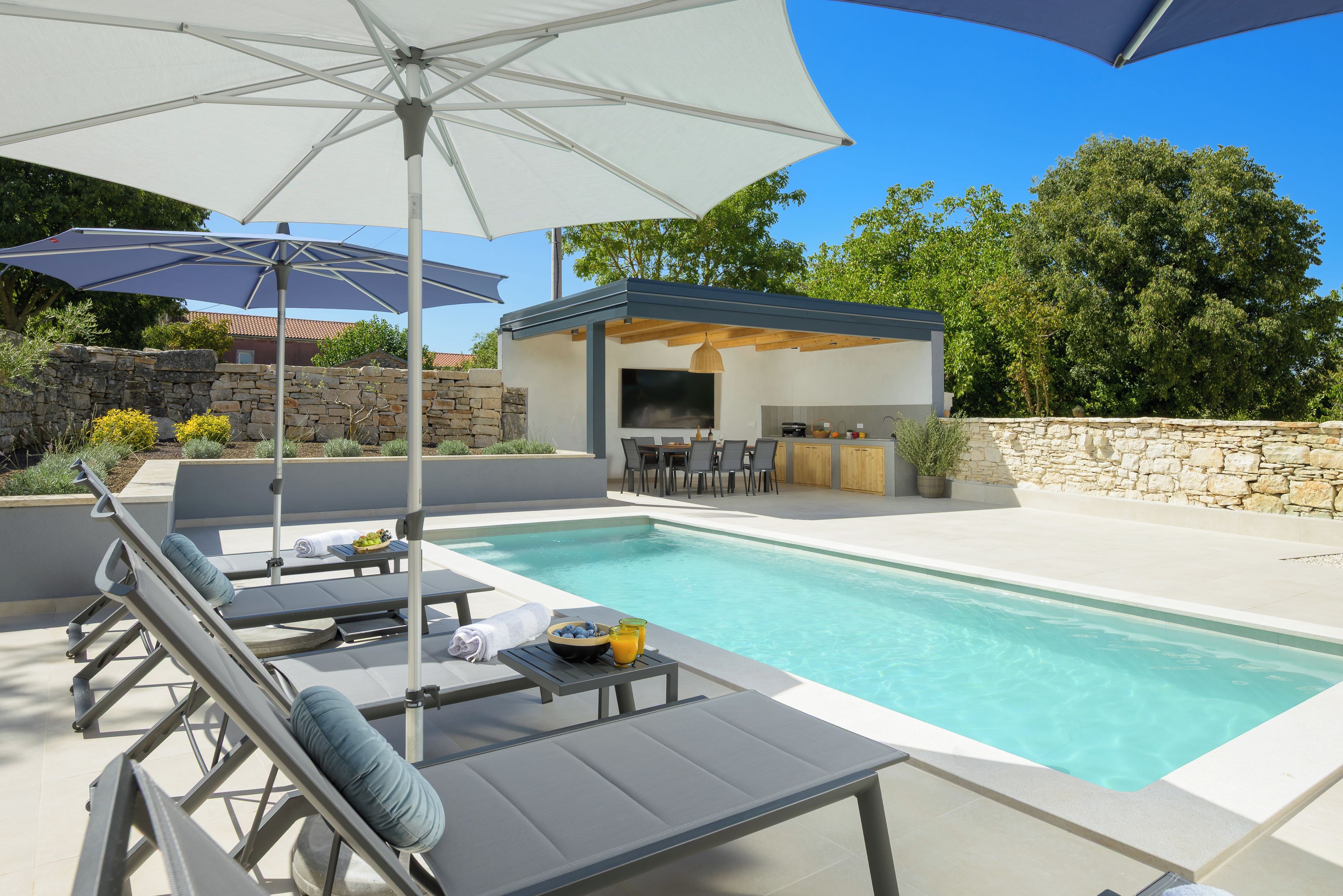 A poolside area with lounge chairs, umbrellas, and a barbecue setup.