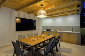 Une cuisine moderne avec un coin repas, un plafond en bois et un téléviseur à écran plat fixé au mur.