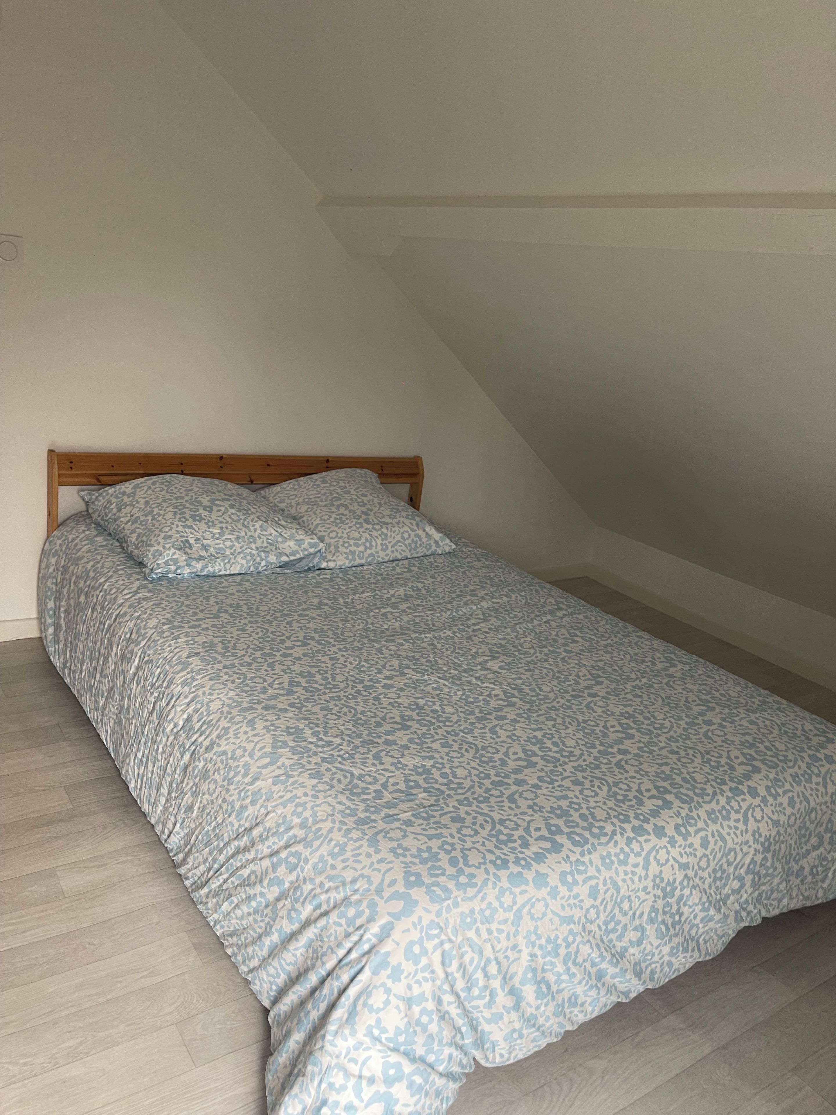 Un letto singolo con un poggiatesta in legno in una stanza con soffitto spiovente.