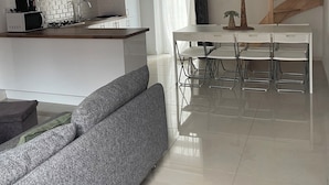 A modern kitchen with white cabinetry, a dining area with a white table and chairs, and a grey sofa.