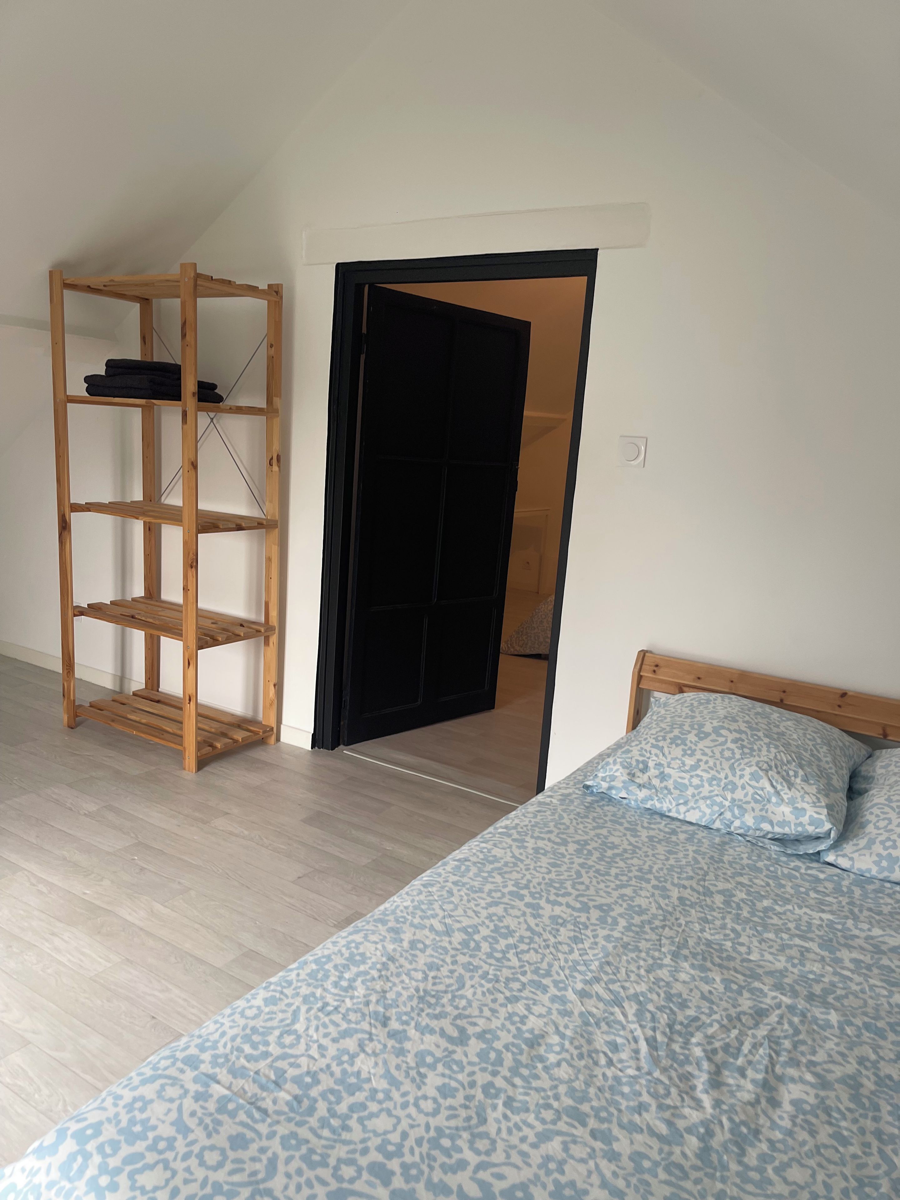 A bedroom with a bed, a wooden shelf unit, and a door leading to another room.
