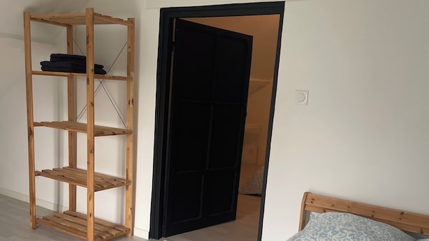 A bedroom with a bed, a wooden shelf unit, and a door leading to another room.