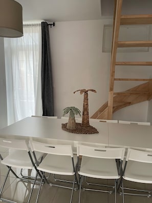 A dining area with a white table, white chairs, a woven palm tree centerpiece, and a wooden ladder against the wall.