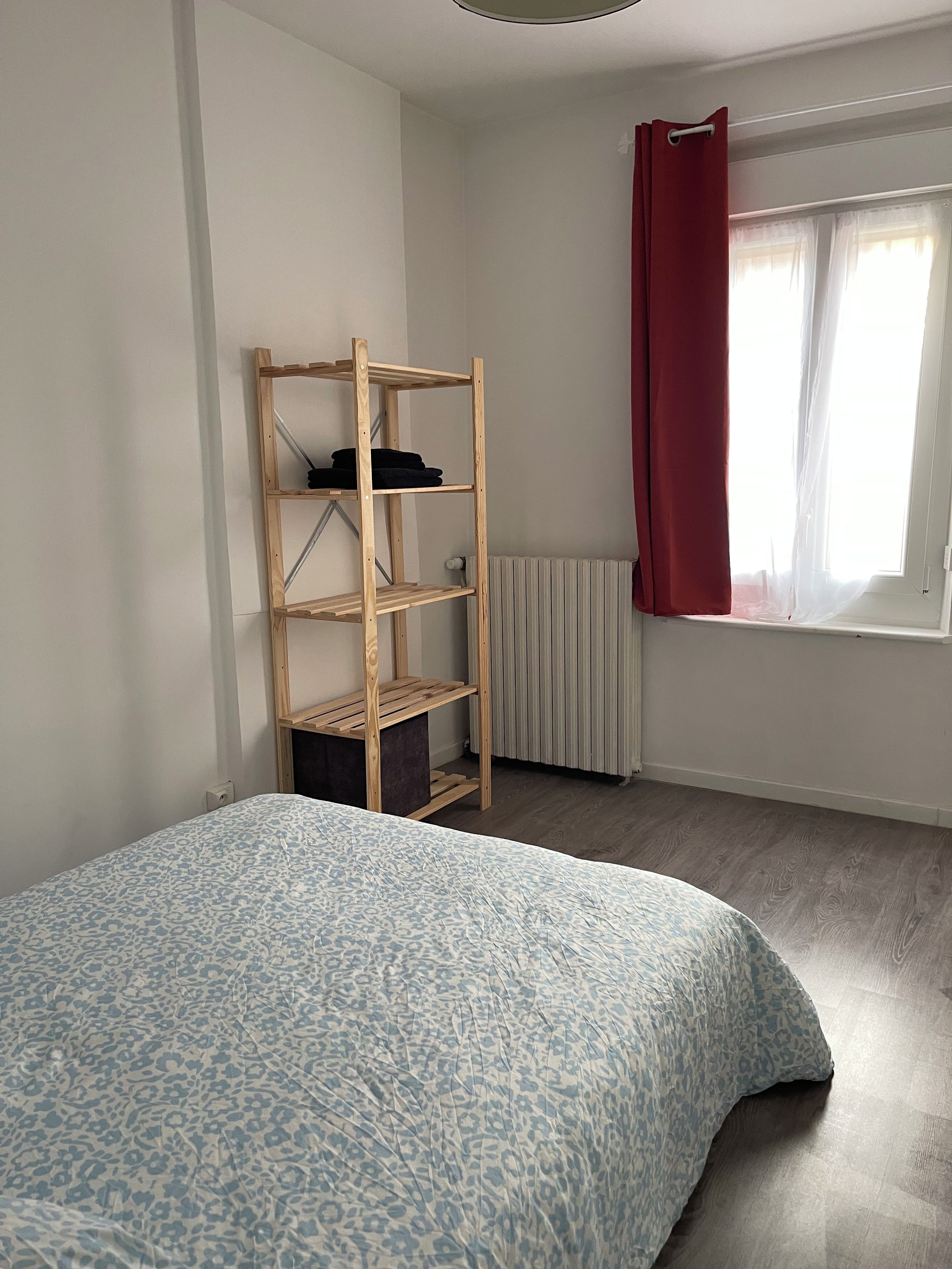 Ein Schlafzimmer mit einem Bett, einer Holzregaleinheit, einem Heizkörper und einem Fenster mit Vorhang.
