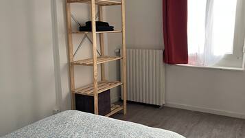 Ein Schlafzimmer mit einem Bett, einer Holzregaleinheit, einem Heizkörper und einem Fenster mit Vorhang.