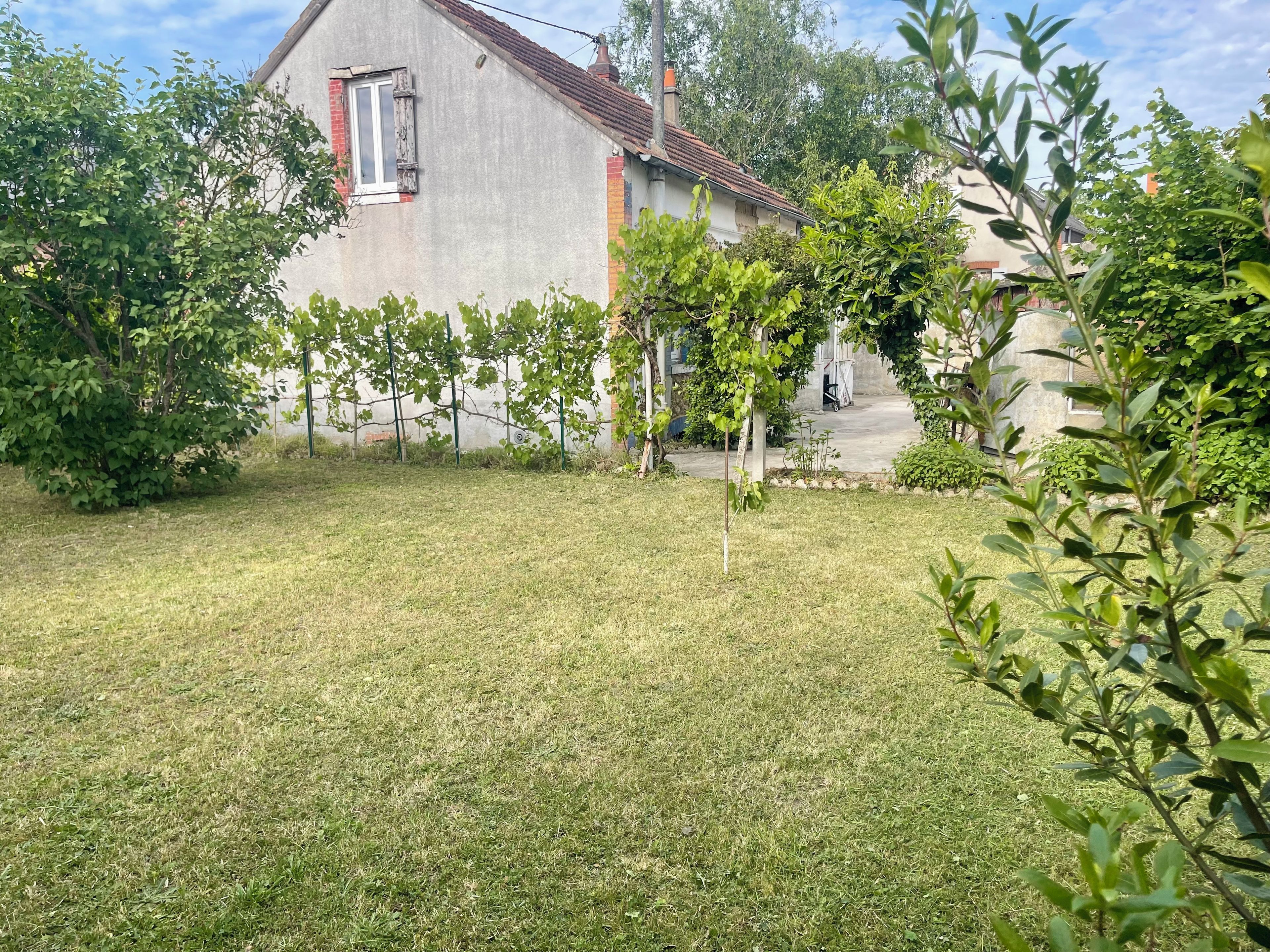 Il s’agit d’une propriété résidentielle dotée d’une cour verdoyante, d’une maison avec un toit recouvert de tuiles rouges et d’un jardin planté de jeunes arbres.