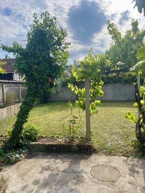 A garden with a concrete patio, a grassy lawn, and a wall in the background. - Tranquil 4-bedroom house in charming Châlette-sur-Loing awaits you (Châlette-sur-Loing)