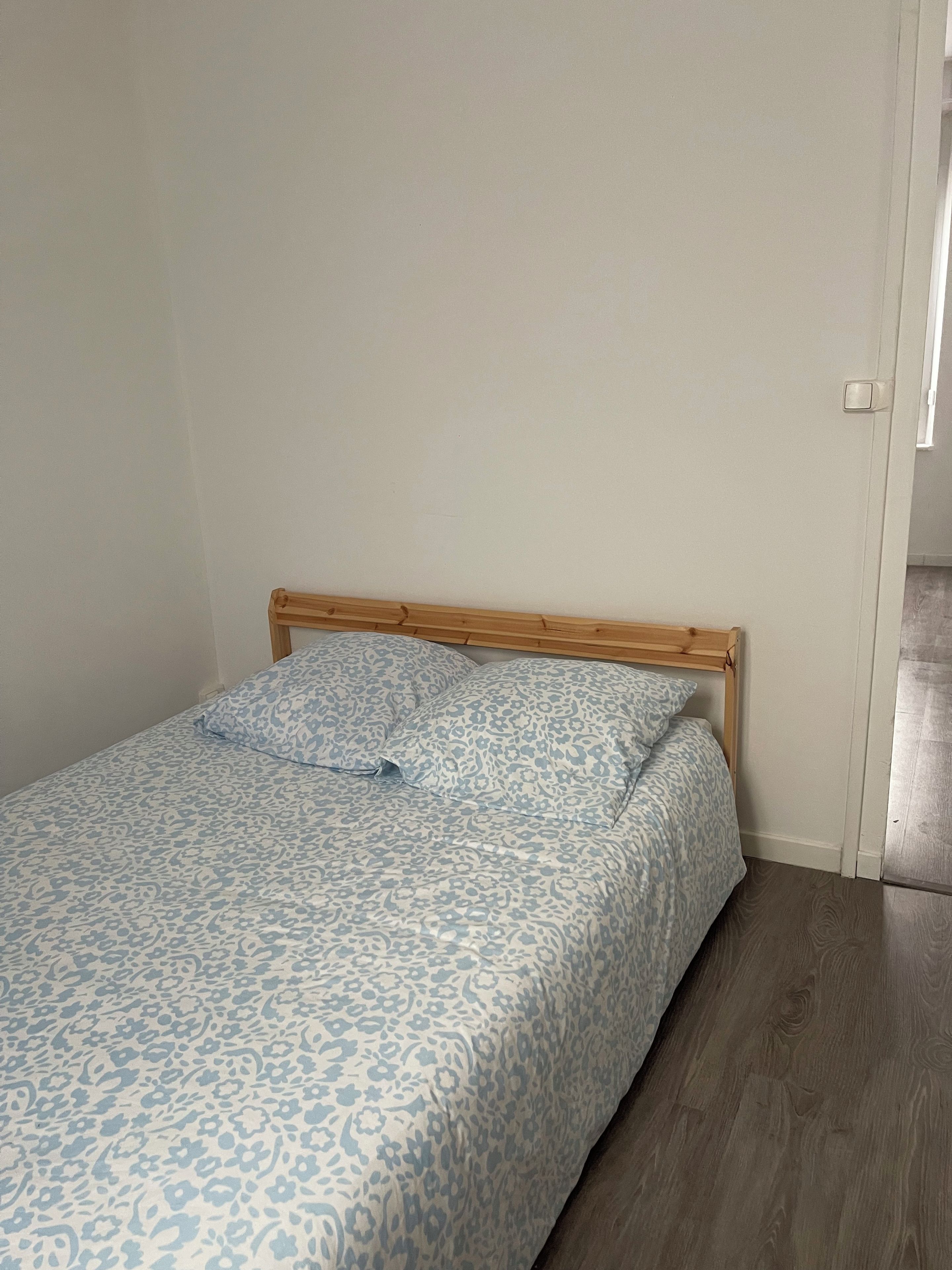 Een eenpersoonsbed met houten hoofdeinde in een kamer met witte wanden en een houten vloer.