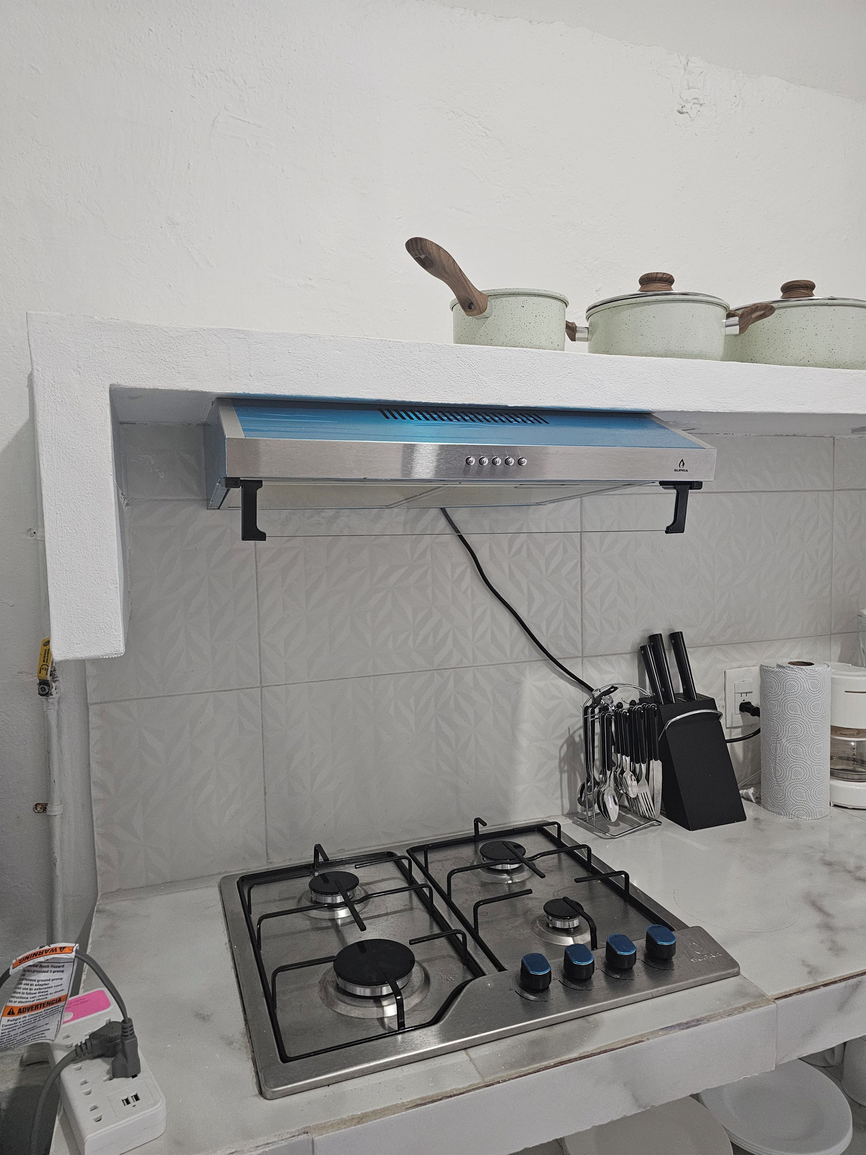 Una cocina con estufa a gas, campana extractora y un colgador de ollas.