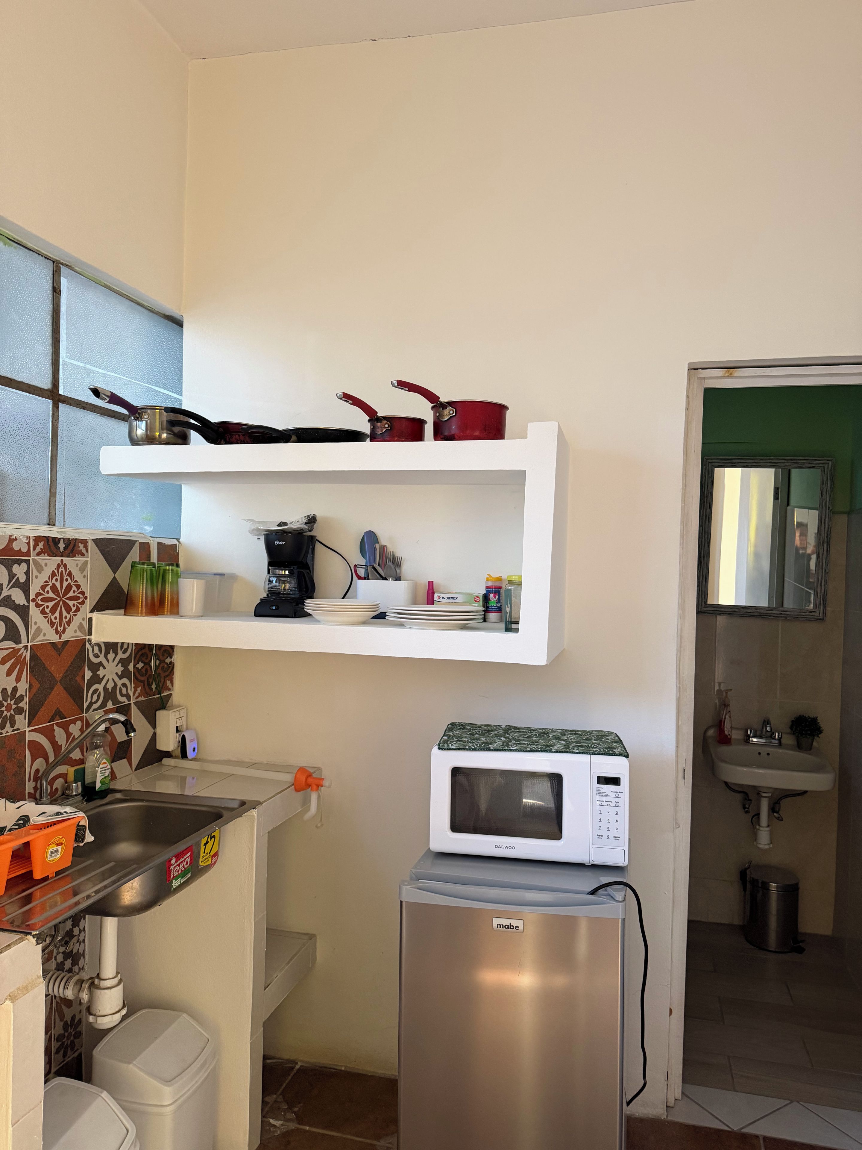 A compact kitchen with a microwave, a refrigerator, a sink, and a shelf with cooking utensils.