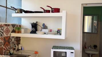 A compact kitchen with a microwave, a refrigerator, a sink, and a shelf with cooking utensils.